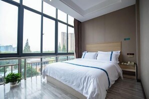 A hotel room with a large window, a bed with white bedding, a wooden headboard, a bedside table, and a potted plant. - Meiyuan Select Hotel (Jingzhou)