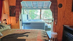 A cozy bedroom with a large bed, a wooden ceiling, and a view of a hot tub outside. - Life is a HOOT in the mountains of Suches (Suches)