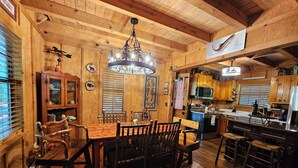 A rustic wooden interior with a dining area, kitchen, and a large chandelier. - Life is a HOOT in the mountains of Suches (Suches)