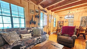 A cozy cabin interior with a wooden ceiling, a sofa with patterned cushions, a wooden coffee table, and a chair with a 'Lodge Life' sign. - Life is a HOOT in the mountains of Suches (Suches)