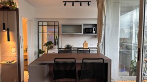 Cocina moderna con una isla central, sillas negras, microondas y vistas al exterior a través de grandes ventanales.