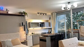 Un espacio habitable moderno y funcional con kitchenette, comedor y un amplio ventanal con vistas al exterior.