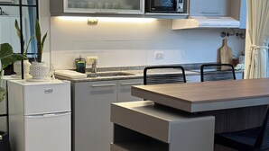Una cocina compacta con microondas integrado, refrigerador y una mesa de comedor de madera con sillas.