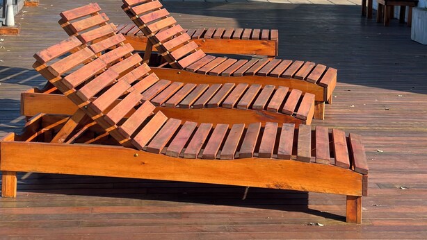 Una terraza de madera con sillones de descanso y una estructura de vidrio.