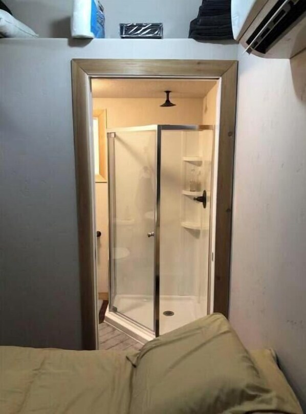 Un couloir étroit mène à un espace de douche clos par des parois de verre, avec un lit au fond.