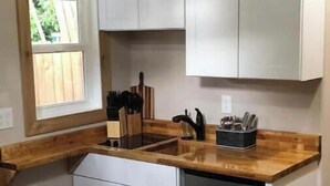 Une cuisine compacte avec des meubles blancs, un plan de travail en bois, un lave-vaisselle et une fenêtre donnant sur un espace verdoyant.