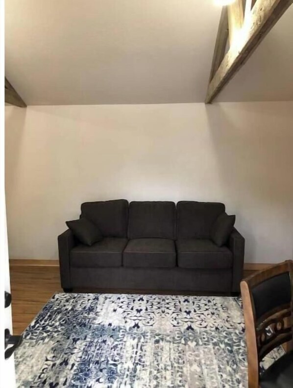 A room with a dark brown sofa against a plain wall, a patterned rug, and a wooden ceiling beam.