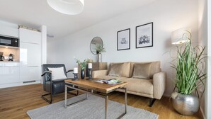 A modern living room with a sofa, a coffee table, a dining table, and a kitchen area in the background.
