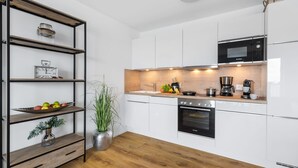 A modern kitchen with white cabinets, a Bosch oven, a microwave, and a coffee maker. There is a wooden floor and a plant on the counter.