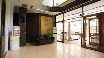 A hotel lobby with a reception desk, a sofa, a vending machine, and a glass door entrance.