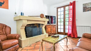 A living room with a stone fireplace, leather armchairs, a wooden cabinet, and a television. - Stunning home in Fournès (Fournès)
