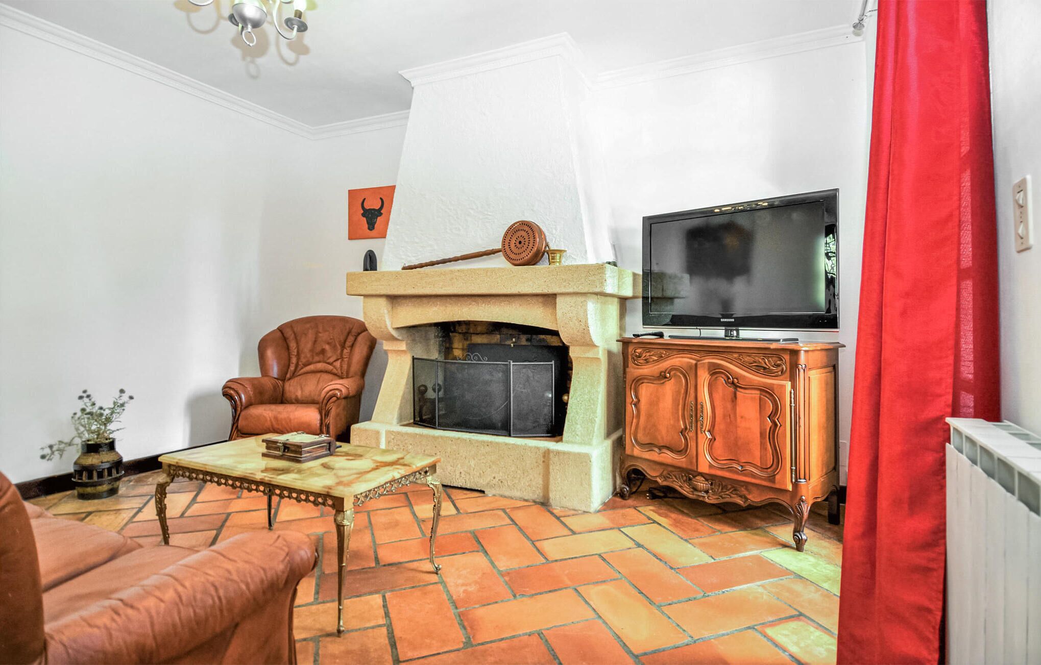 A living room with a fireplace, a television, a leather armchair, and a red curtain.