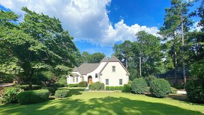 A two-story house with a well-maintained lawn and a variety of trees and shrubs.