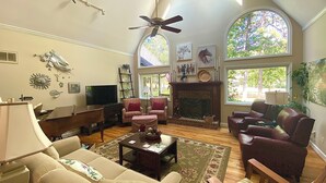A spacious living room with high ceilings, a fireplace, and large windows.