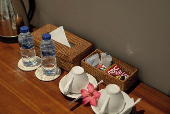 A table with two water bottles, two white cups, a pink flower, and a basket containing magazines. - Warsa's Garden Bungalow and Spa (Bali)