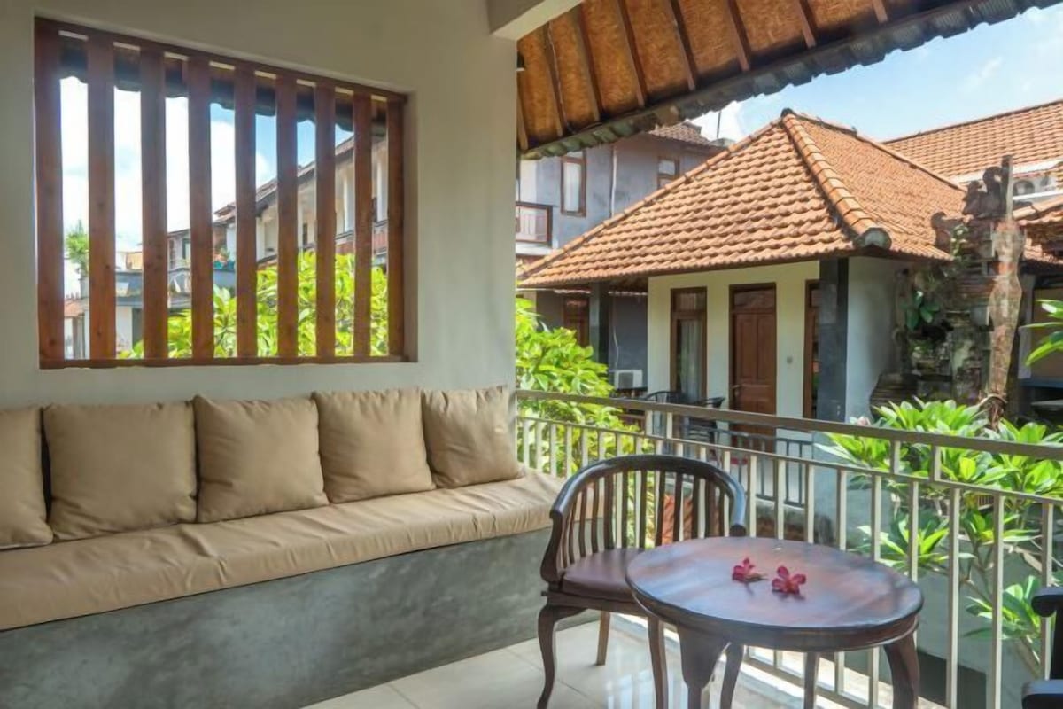 A balcony with a sofa and a small table, overlooking a residential area with houses and greenery.