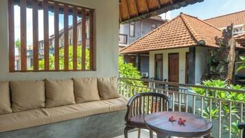 Varanda com sofá e uma pequena mesa, com vista para uma área residencial com casas e vegetação.
