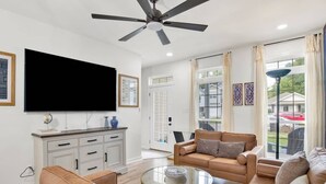 Un salon spacieux doté d’un ventilateur de plafond, d’un téléviseur à écran plat, d’une table basse en verre et d’un canapé beige.
