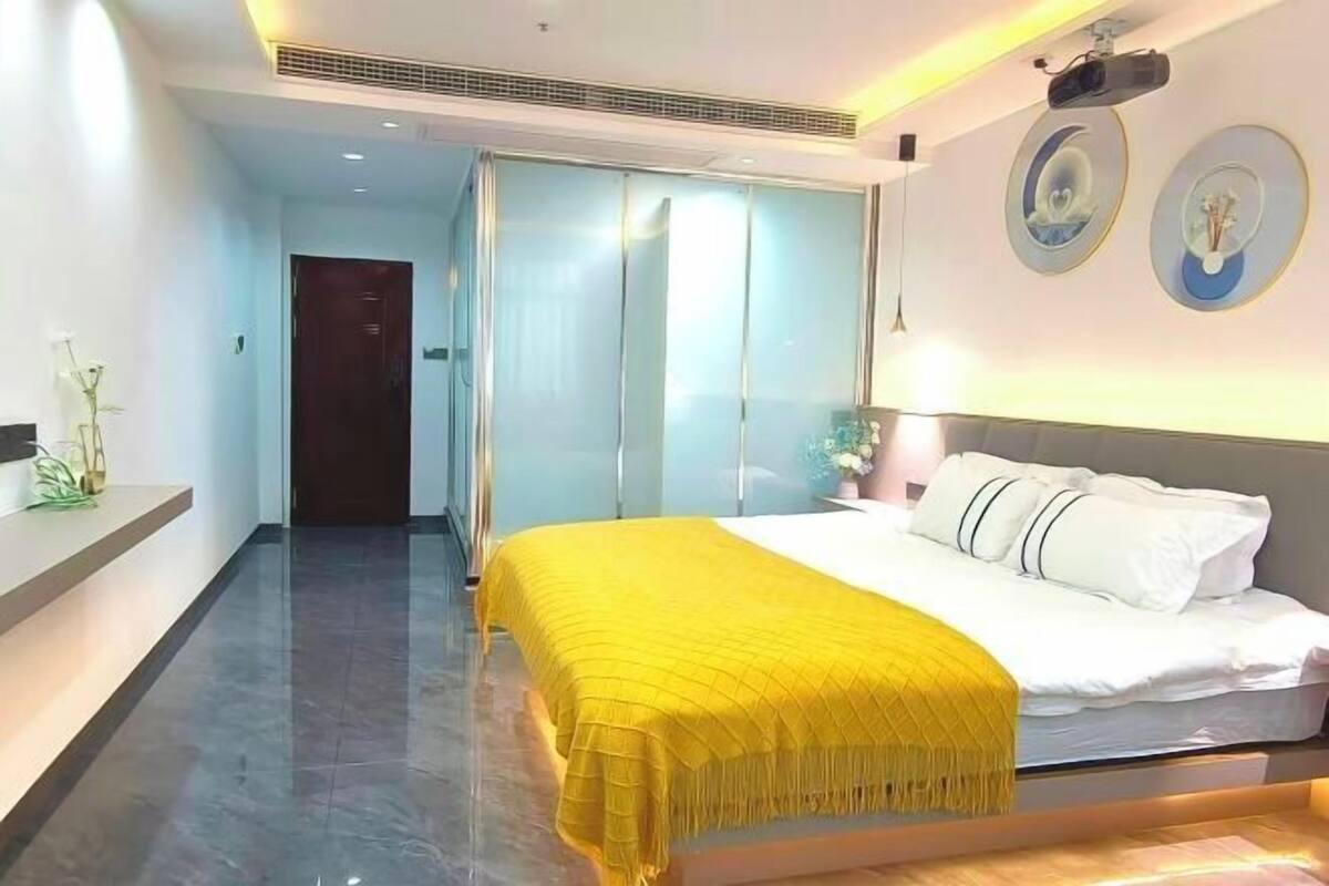 Ein modernes Hotelzimmer mit Bett, Nachttisch, Spiegel und einem an der Wand befestigten Projektor.