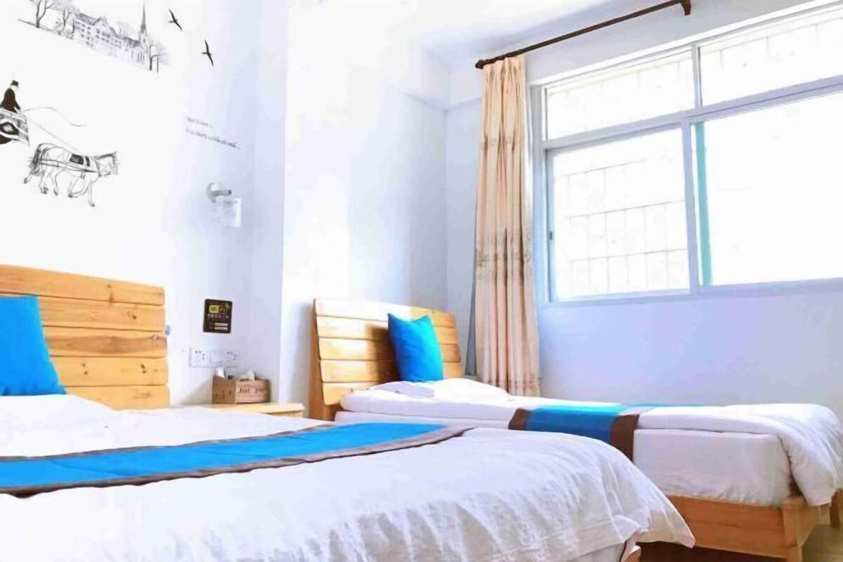 Ein Zimmer mit zwei Betten, einem hölzernen Kopfteil, einem Fenster mit Vorhängen und einer Wand mit Wandgemälde.