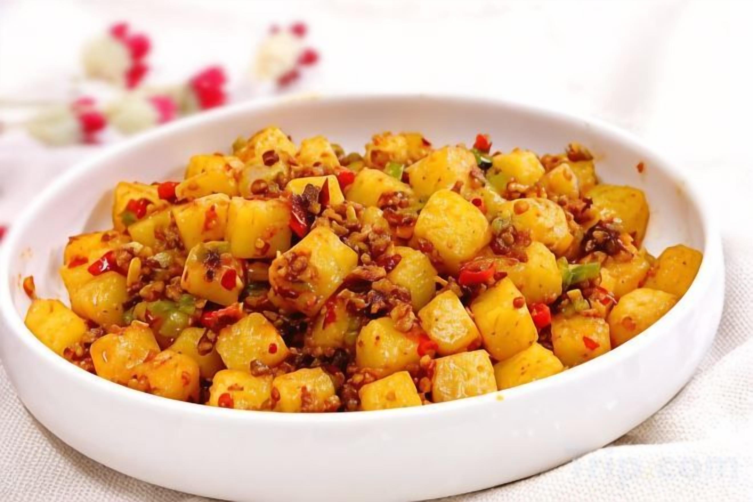 Un tazón blanco lleno de papas en cubos, pimientos rojos y carne molida.