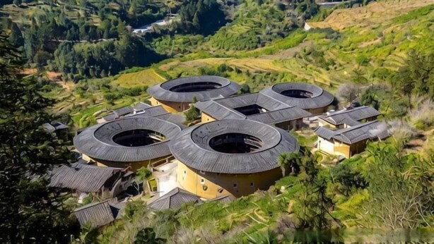 A cluster of traditional round-roofed buildings with a central courtyard, surrounded by terraced fields and forested hills. - YunShuiYao Tian'e Hotel (Nanjing County)
