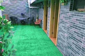 Une terrasse avec une pelouse artificielle verte, un mur en briques et une porte en bois.