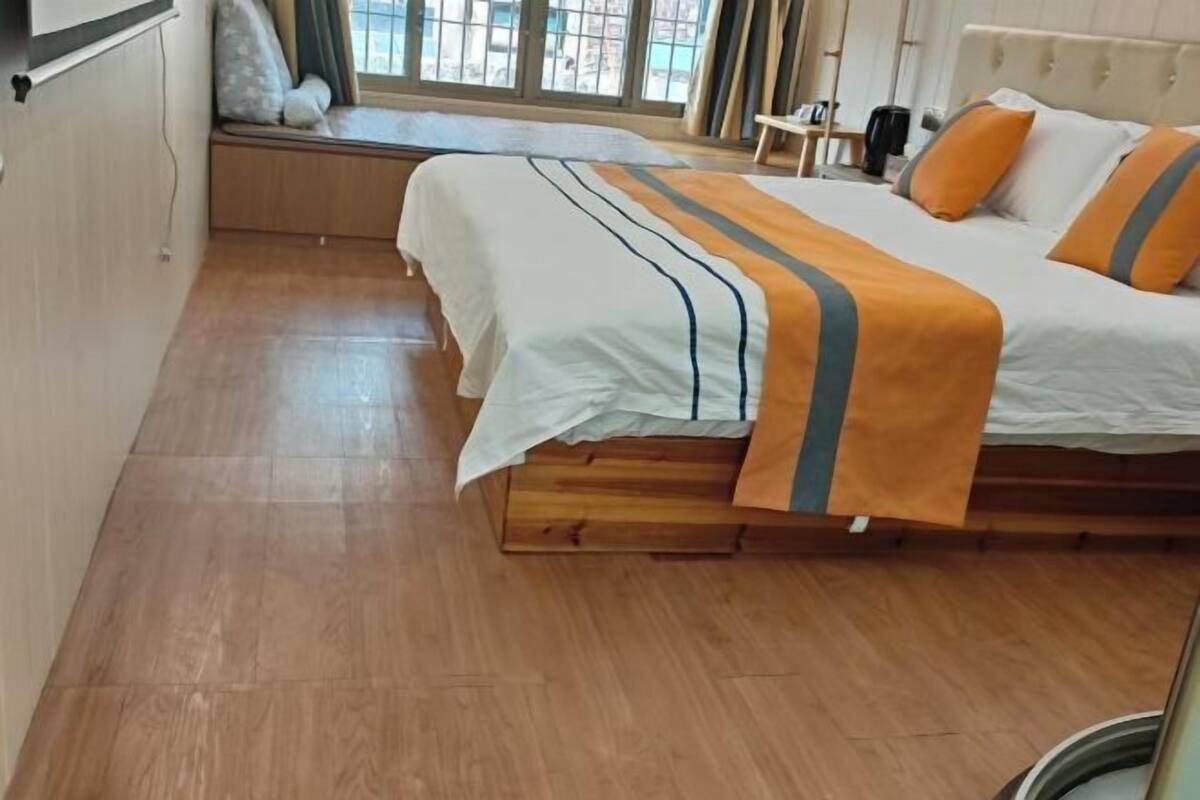 Ein Schlafzimmer mit Bett, Holzboden, Fensterbank und Blick ins Freie.