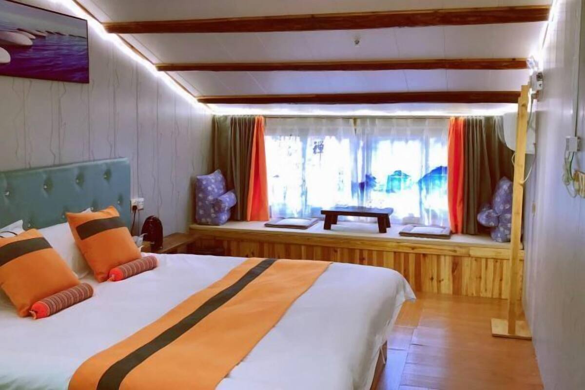 Ein Hotelzimmer mit Bett, Holz-Kopfteil, einer Sitzbank am Fenster und Blick ins Freie.