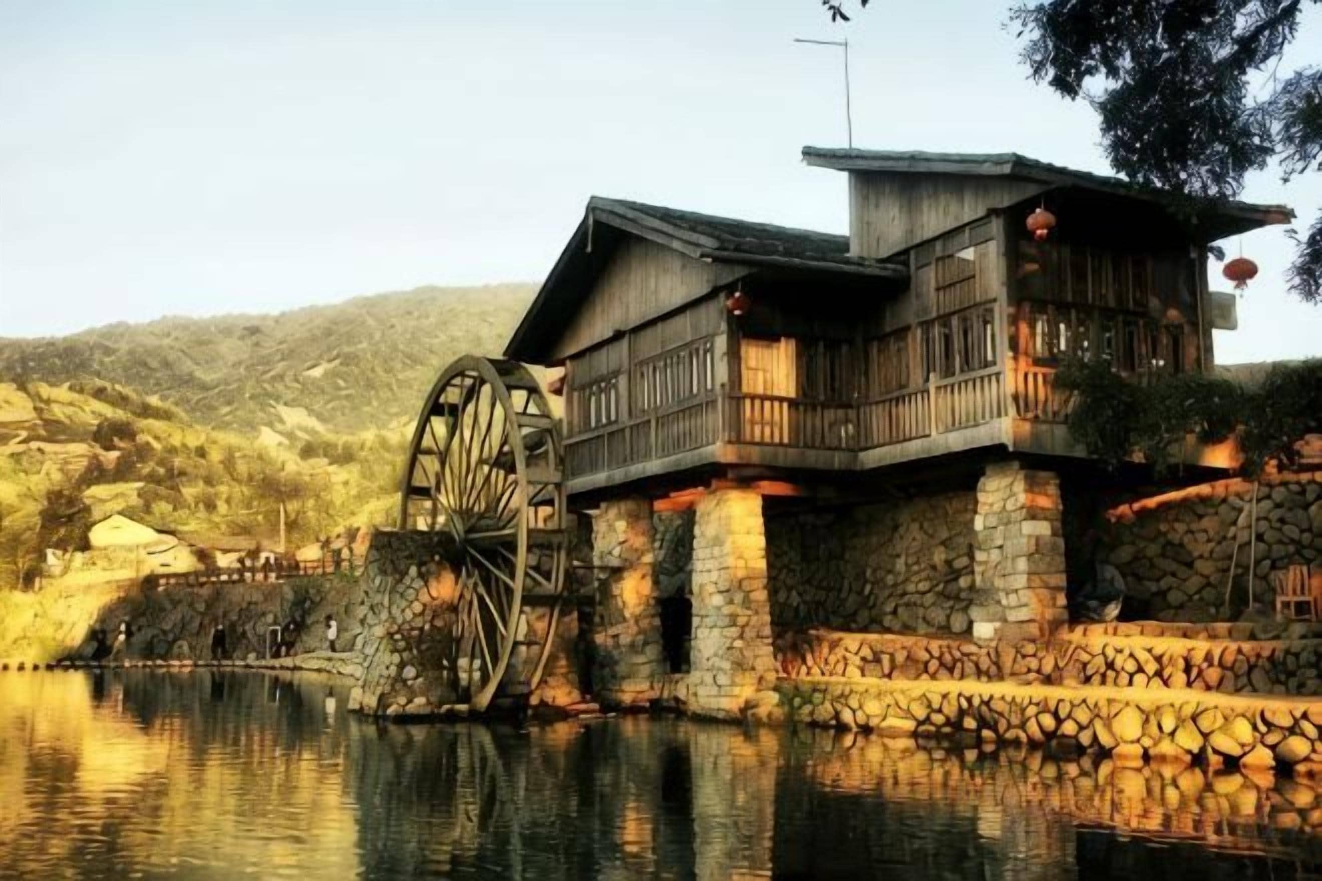 A traditional wooden building with a water wheel, stone walls, and a balcony.