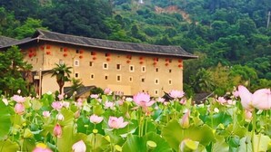 A traditional building with a tiled roof, surrounded by lush greenery and lotus flowers. - YunShuiYao Tian'e Hotel (Nanjing County)
