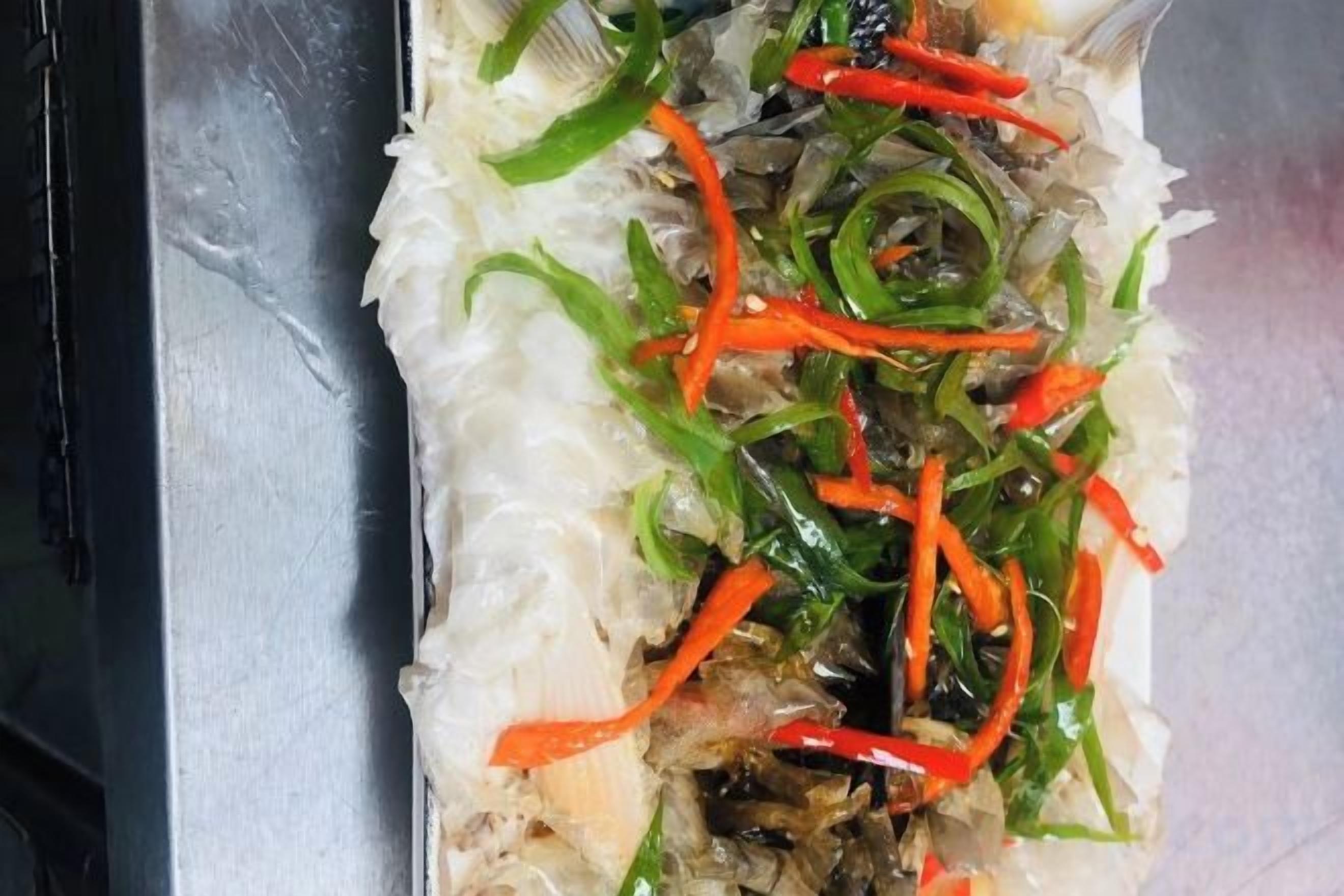 A tray with shredded white vegetable, possibly cabbage, topped with sliced red and green bell peppers.