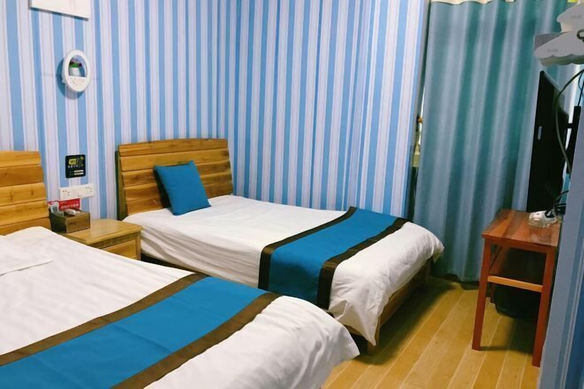 Une chambre d’hôtel avec deux lits, des murs rayés bleus et blancs, une tête de lit en bois, une petite table et un téléviseur.