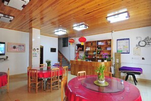 Un restaurant avec un plafond en bois, une table ronde recouverte d’une nappe rouge et un comptoir avec des étagères.