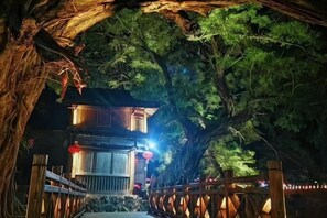 Ein Weg führt zu einem Gebäude im traditionellen Baustil, umgeben von Bäumen und beleuchtet durch warmes Licht.