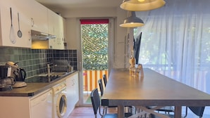 Une cuisine moderne équipée d’un lave-linge intégré, un coin repas avec des chaises et une vue sur l’extérieur par une fenêtre.