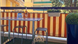 Un balcon avec une table, deux chaises, une bouteille de vin et une plante en pot.