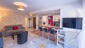 Un salon moderne avec un canapé, une table basse et un téléviseur. Il y a également un coin cuisine avec un bar et une table à manger.