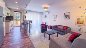 Un salon moderne avec un canapé, une table basse et des fauteuils. Il y a également un coin cuisine avec une table à manger et des chaises. La pièce est dotée de grandes fenêtres et offre une vue sur l'extérieur.