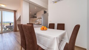 Un comedor con una mesa preparada para cuatro personas, una cocina al fondo y vistas a través de una puerta de vidrio.