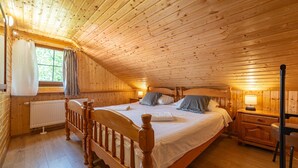 Un dormitorio acogedor de cabaña de madera con una cama grande, una mesita de noche, una silla y una ventana con cortinas.