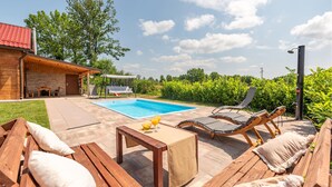 Terraza de madera con piscina, sillas de descanso y una mesa con bebidas.