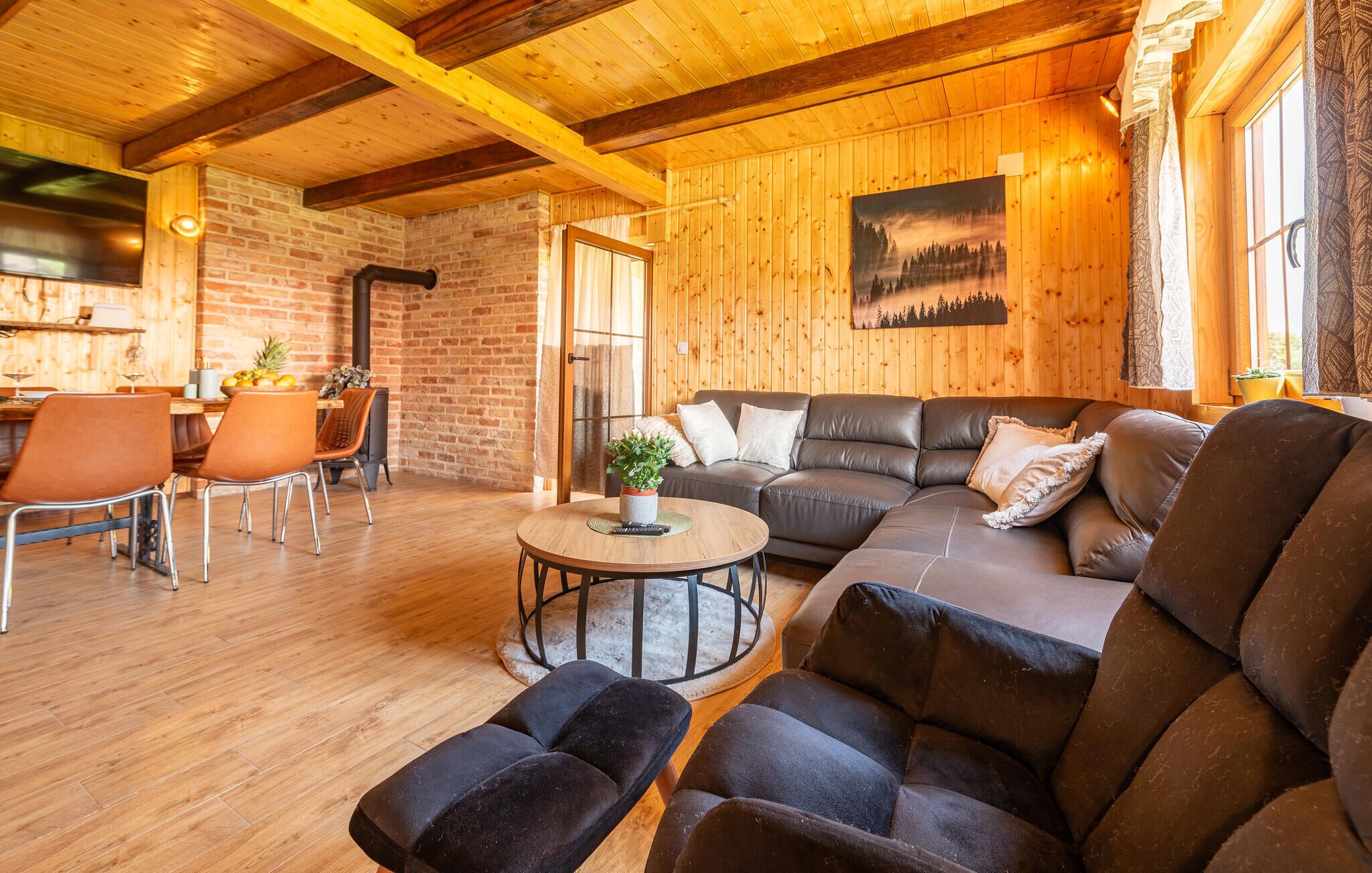 Een gezellige woonkamer met een houten plafond, een open haard, een bank en een eethoek met stoelen.