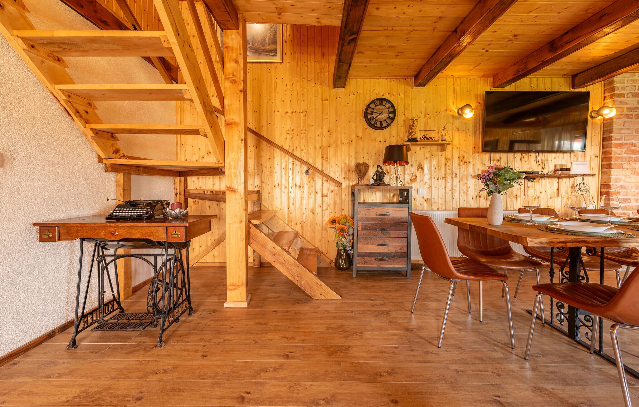 A wooden interior with a staircase, a dining area with chairs, a table, and a kitchen area with a stove.