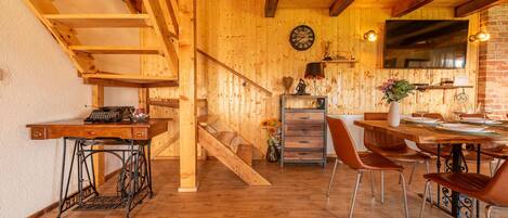 A wooden interior with a staircase, a dining area with chairs, a table, and a kitchen area with a stove.