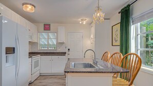 Una cocina moderna con armarios blancos, encimera de granito, lavaplatos integrado y zona de comedor con sillas de madera.