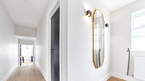 Un pasillo con piso de madera, una puerta negra y una pared blanca con espejo de marco dorado.
