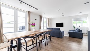 Una sala de estar moderna con una mesa de comedor de madera, dos sofás y un televisor de pantalla plana montado en la pared.