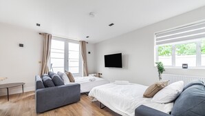 Una habitación de hotel moderna con dos camas, un sofá, un televisor de pantalla plana y un ventanal con cortinas.