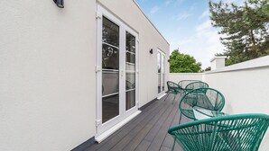 A building with a white exterior, large windows, and a deck area with green metal chairs.